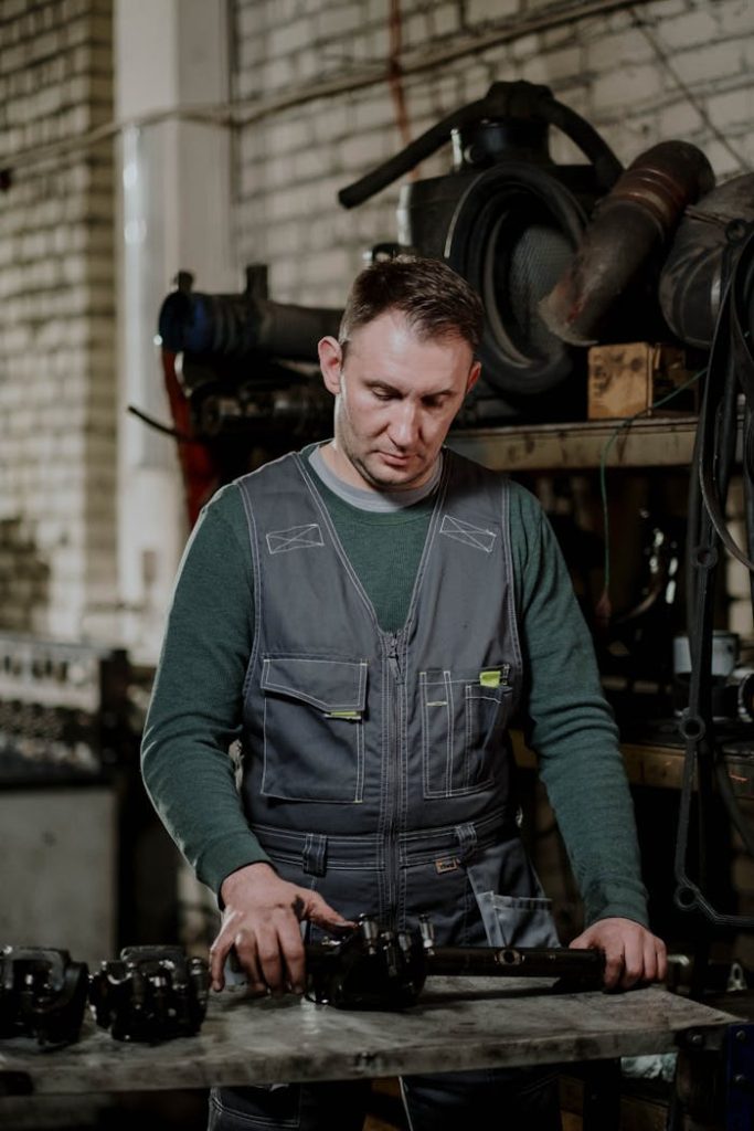 Mechanic focuses on repairing car parts in an industrial workshop setting.